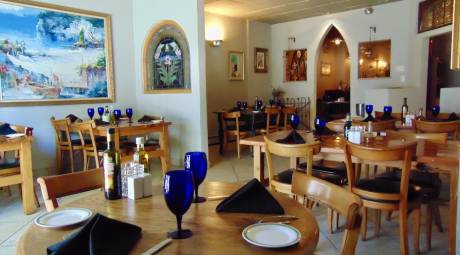 Inside of the dining room at Positano Ristorante. Blue drinking glasses are placed on each table with a folded navy blue napkin and appetizer plate with silverware.