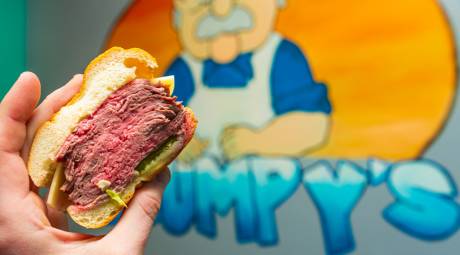 Hand holding a roast beef sandwich in front of the Grumpy's Handcarved Sandwiches logo