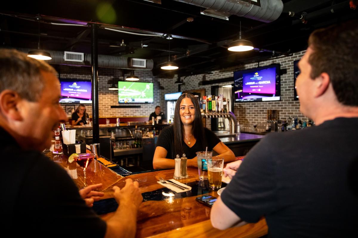 Female bartender at King of Prussia Grill & Tavern talks to two customers sitting at the bar