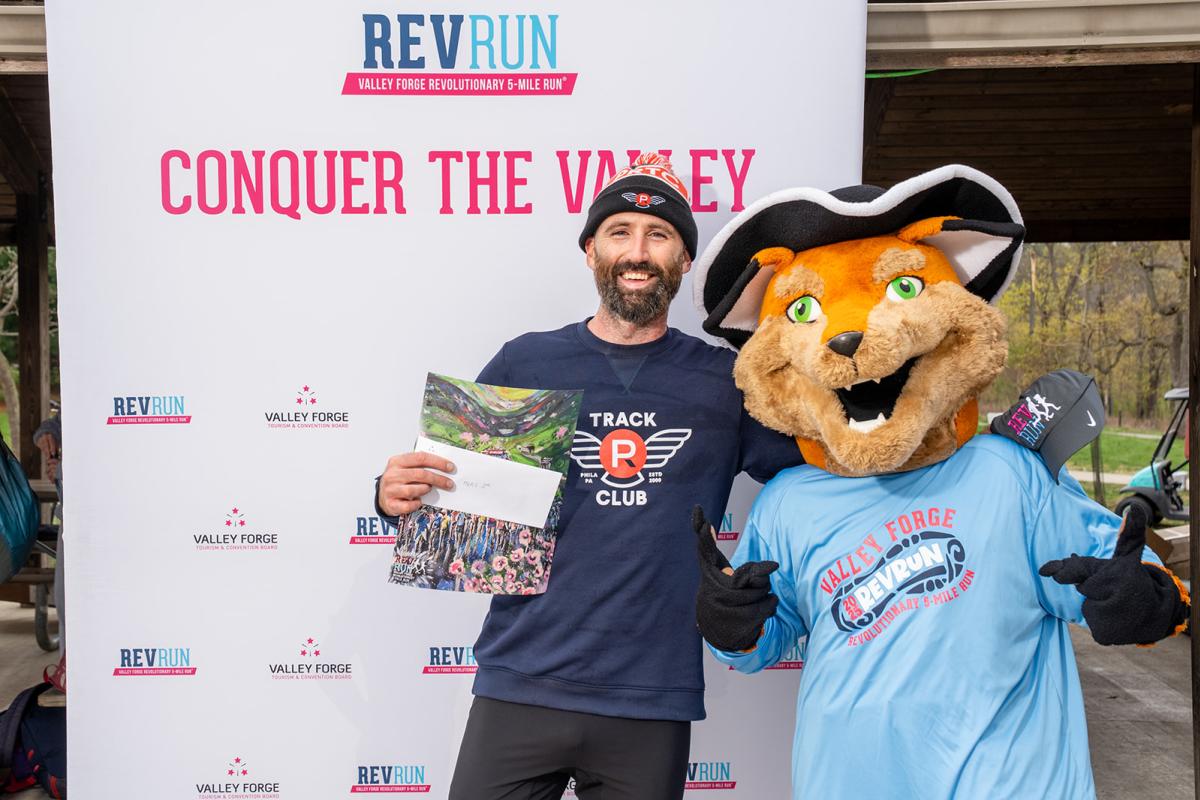 Male smiles with a mascot receiving a Rev Run award
