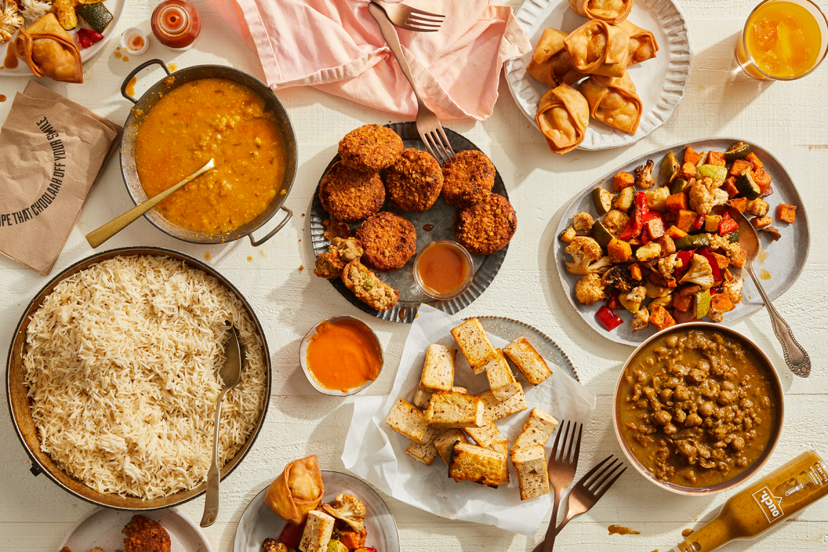 Colorful Choolaah Indian BBQ dishes with basmati rice, samosas, and vibrant sides displayed on a white table.