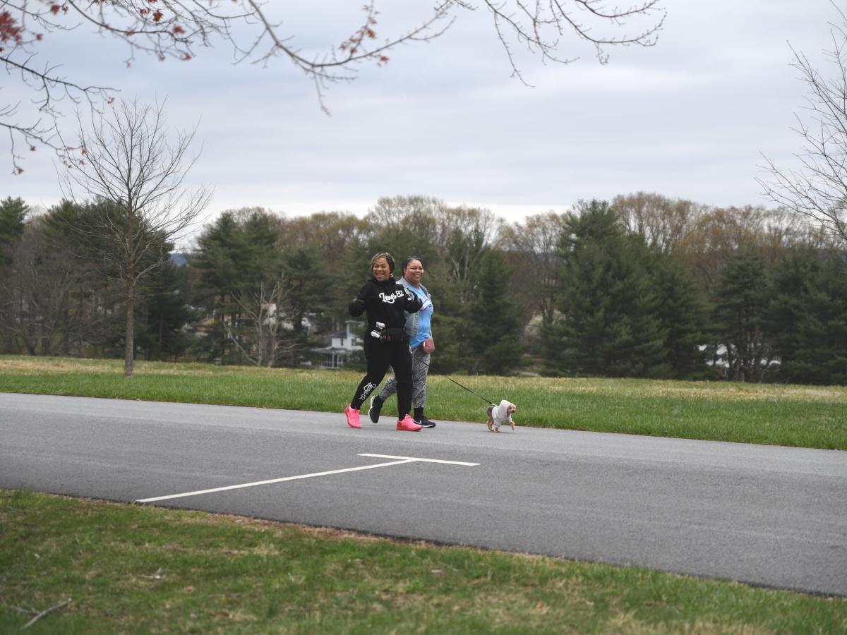 Two females smile while walking a leashed dog at the Rev Run 2-Mile Walk