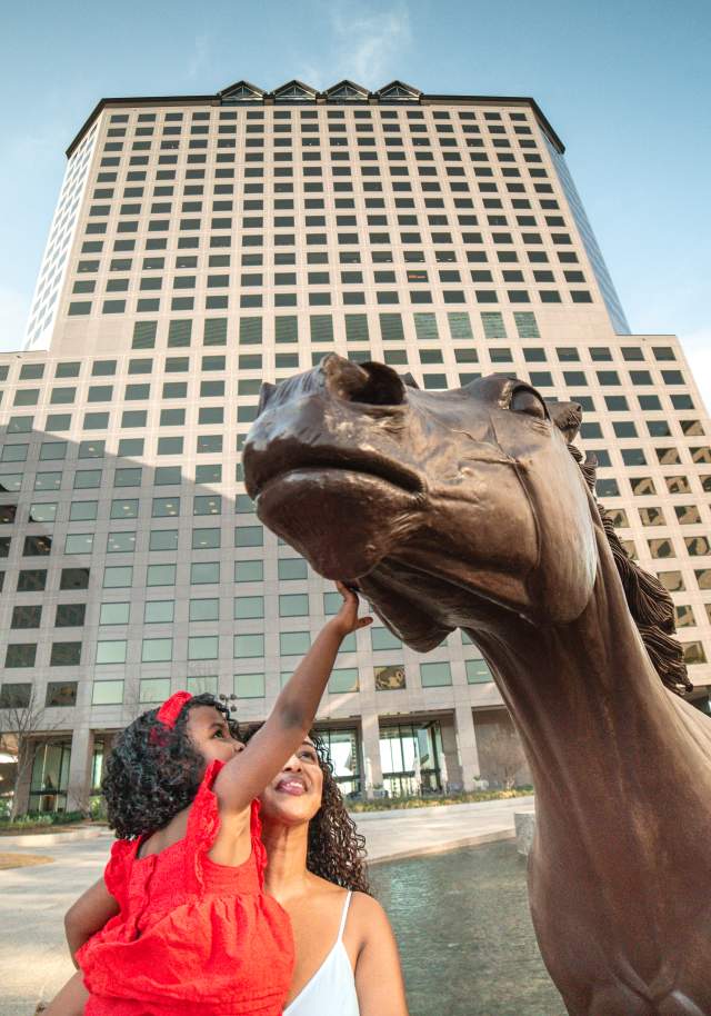 Little girl reaching for Mustang Statue