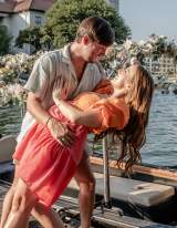Couple shares joyful moment on dock beside floral-adorned gondola, celebrating with champagne by waterfront