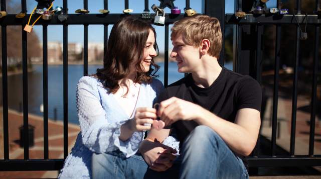 Couple smiles and holds heart-shaped lock on Love Lock Bridge in Irving Texas.