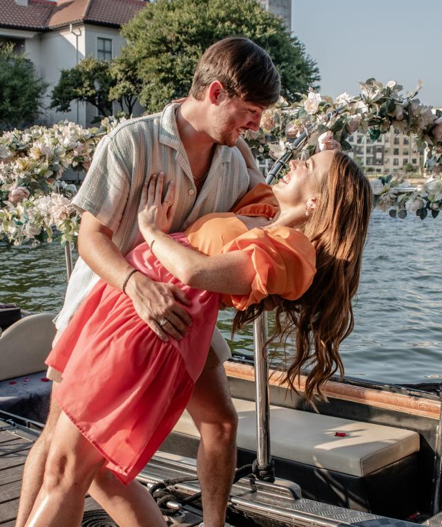 Couple shares joyful moment on dock beside floral-adorned gondola, celebrating with champagne by waterfront