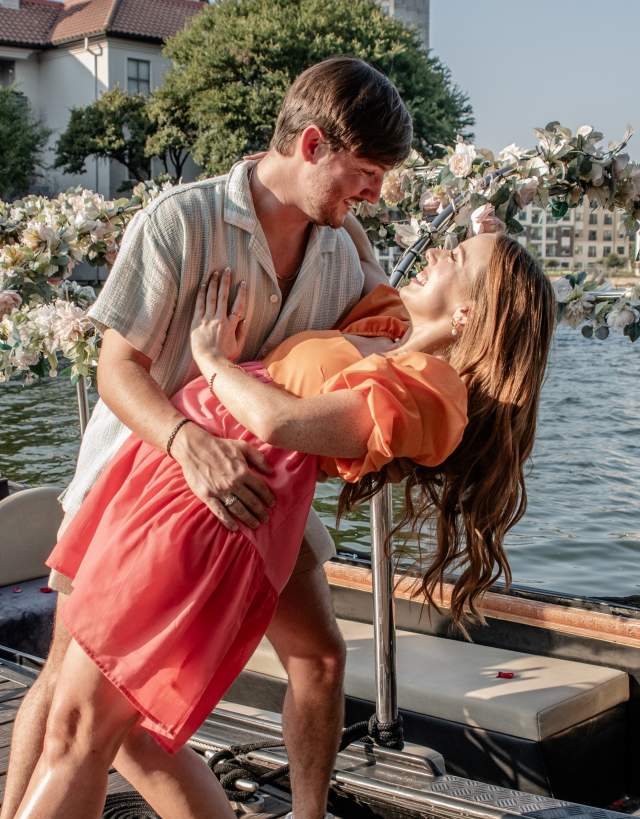 Couple shares joyful moment on dock beside floral-adorned gondola, celebrating with champagne by waterfront