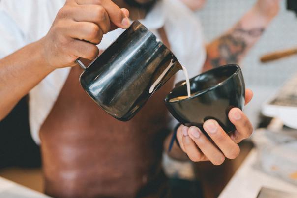 A Barista artfully pours steamed milk into a fresh cappuccino at Pax & Beneficia Coffee