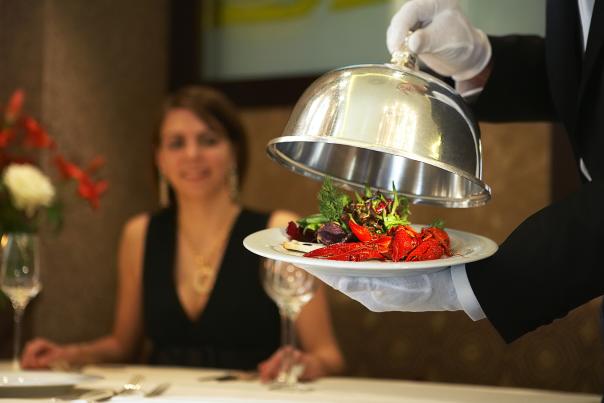 A guest looks on as a waiter presents a lobster main course.