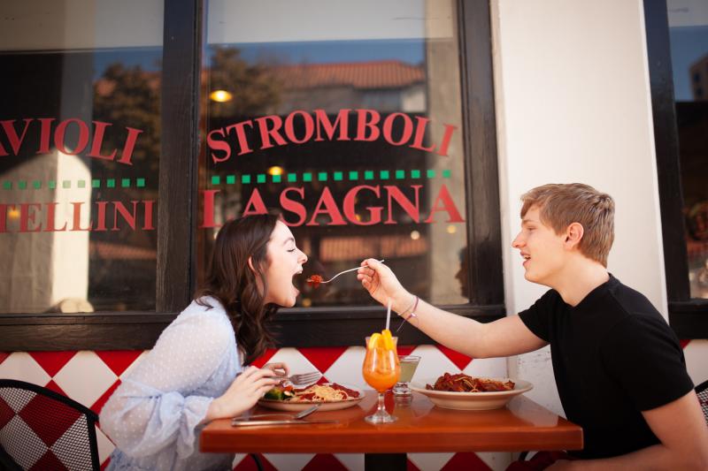 Man feeds woman a bite of pasta on outdoor patio of Italian Cafe
