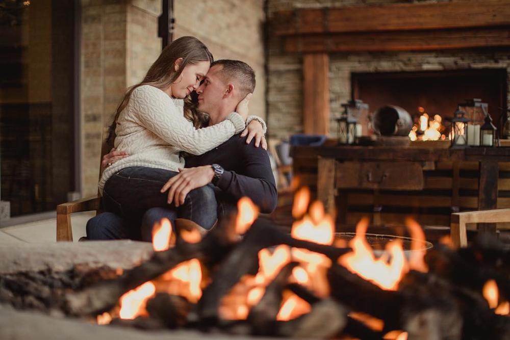 Woman sitting on man's lap, sharing a romantic moment, near a cozy fire