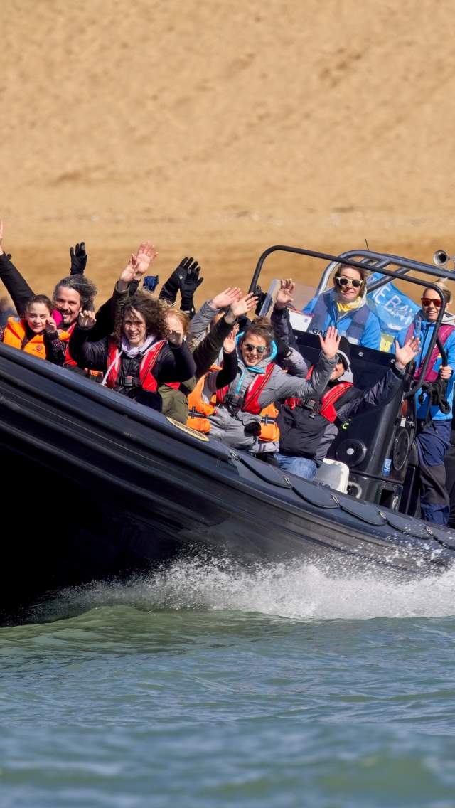 A RIB boat ride at West Bay in Dorset with passengers holding their arms up in the air as the boat speeds through the water