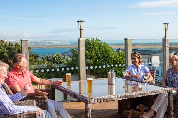 Four people enjoying a drink on the outdoor terrace bar at Chesil Beach Holiday Park in Dorset