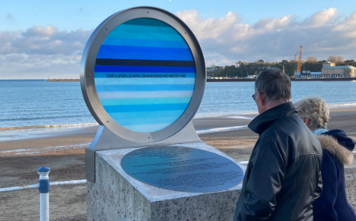 Two people looking at the Levels sculpture on Weymouth seafront