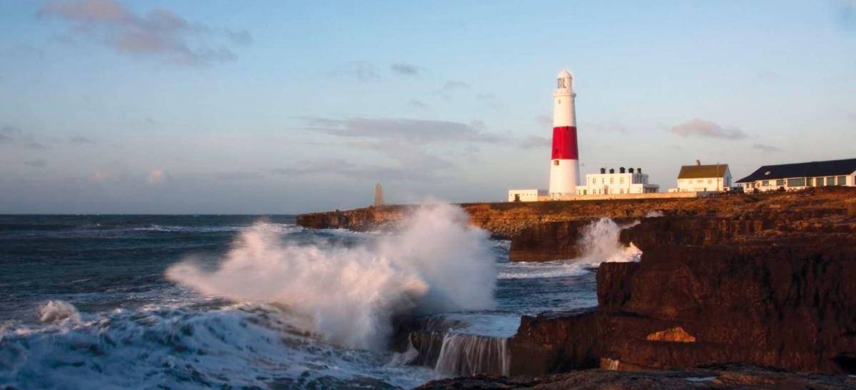 The red and white lighthouse at Portland Bill in Dorset, located next to a rocky coastline with waves crashing against the shore