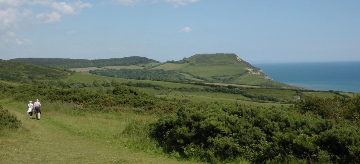 Two people walking at Stonebarrow, with a view of the Dorset coast in the distance