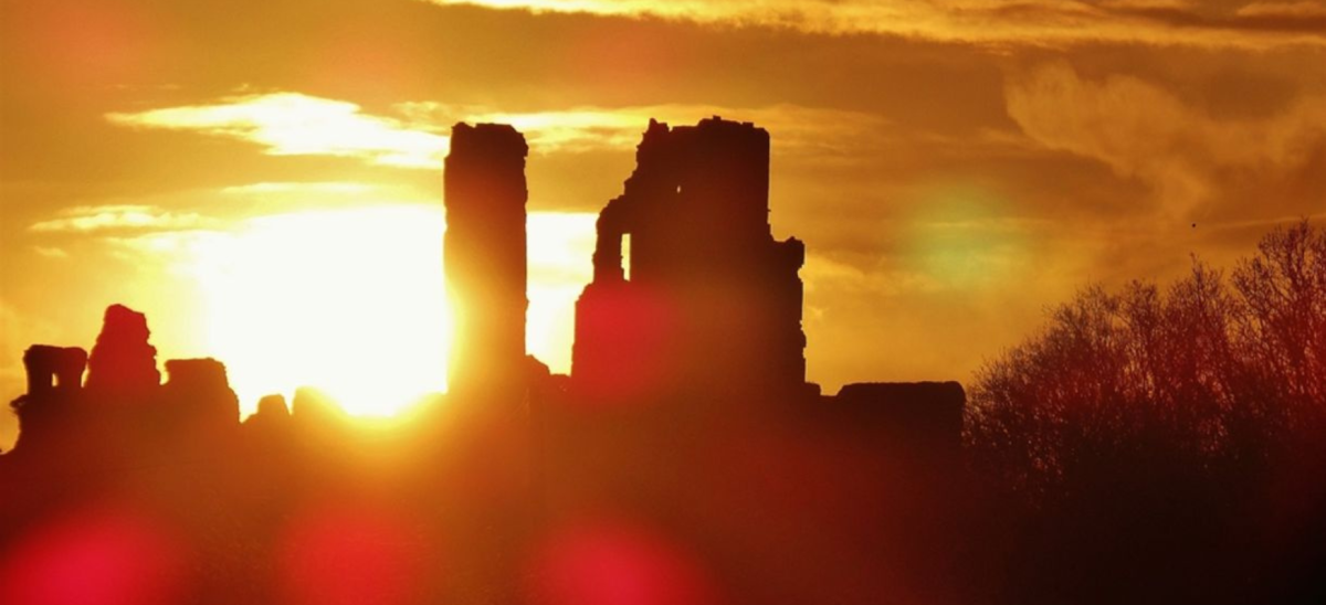 Sun rising behind Corfe Castle, which is in shadow.